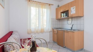 A compact kitchen with wooden cabinets, a microwave, and a sink. There is a dining table with a floral tablecloth and a pitcher of water. - Apartment in Orebić with Balcony, Air condition, WIFI, Dishwasher (4934-6) (Orebic)