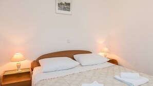 A neatly made bed with white linens and pillows, two bedside lamps, a small wooden nightstand, and a framed picture on the wall. - Apartment in Orebić with Seaview, Balcony, Air condition, WIFI (4934-7) (Orebic)