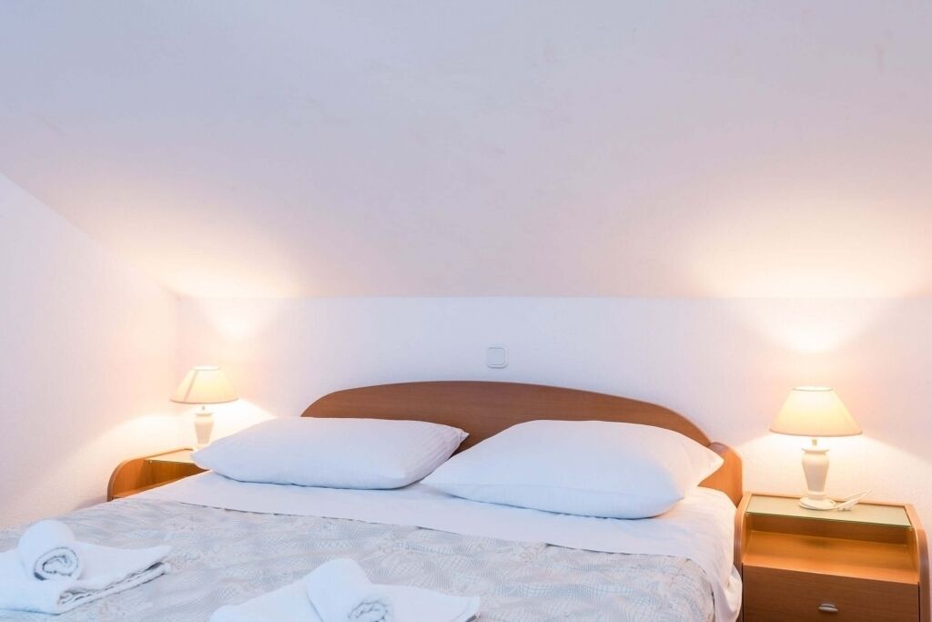 A neatly made bed with white linens and pillows, two bedside lamps, and a wooden headboard.
