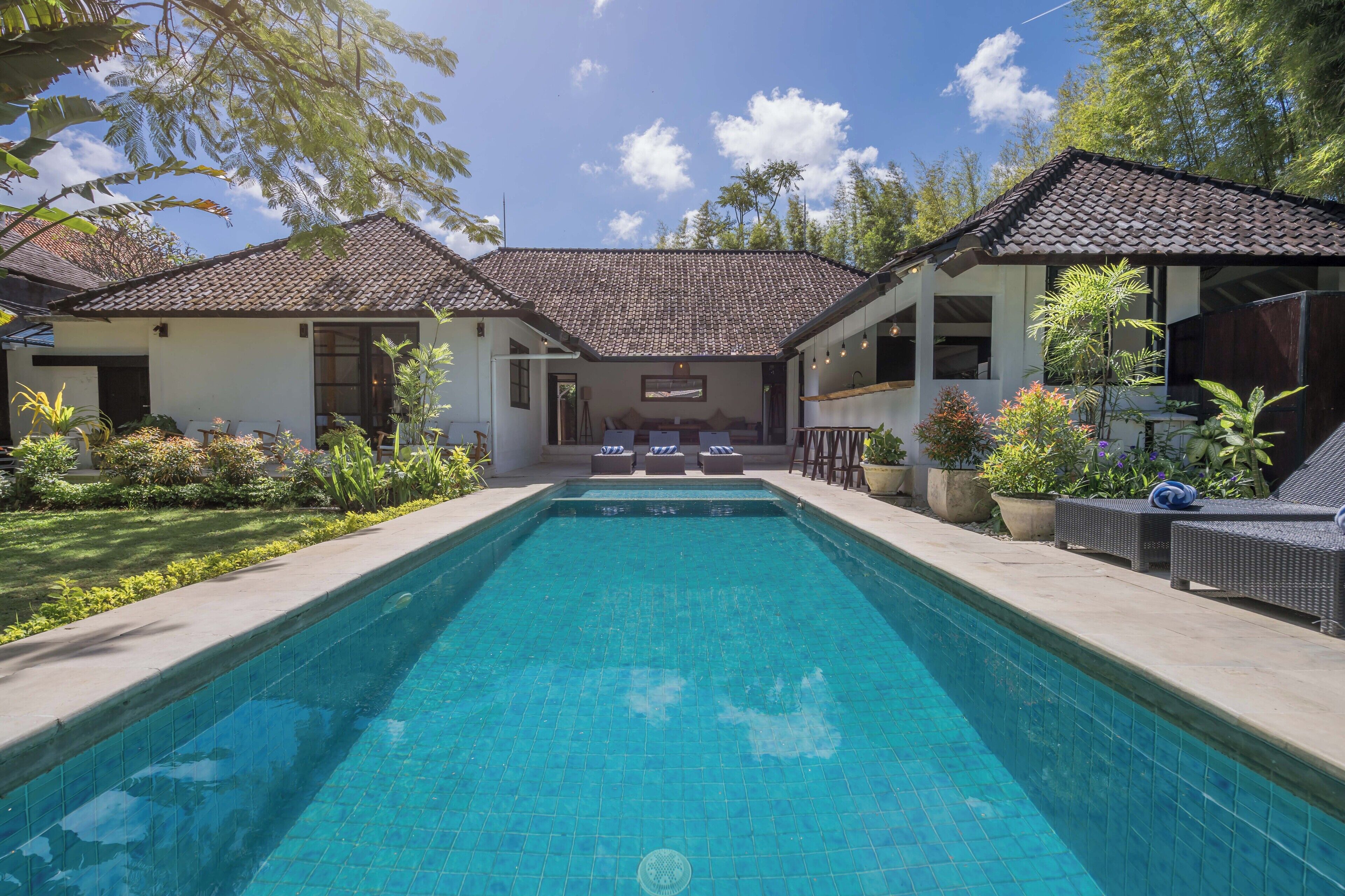 A pool with lounge chairs and a covered seating area, surrounded by greenery.