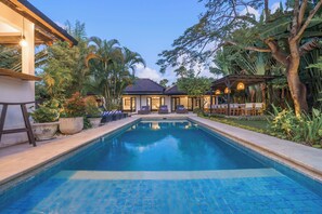 A swimming pool with lounge chairs and a covered seating area, surrounded by tropical vegetation. - LARGE GROUPS, 10 BDR, NR BEACH, GREAT INCLUSIONS (Seminyak)