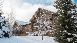 A two-story building with a stone facade, surrounded by snow-covered trees and a clear sky.