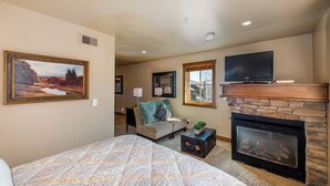 A bedroom with a large bed, a fireplace, a television, and a painting on the wall.