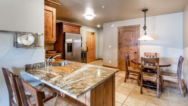 A kitchen with granite countertops, wooden cabinets, a stainless steel refrigerator, and a dining area with wooden chairs and a table.