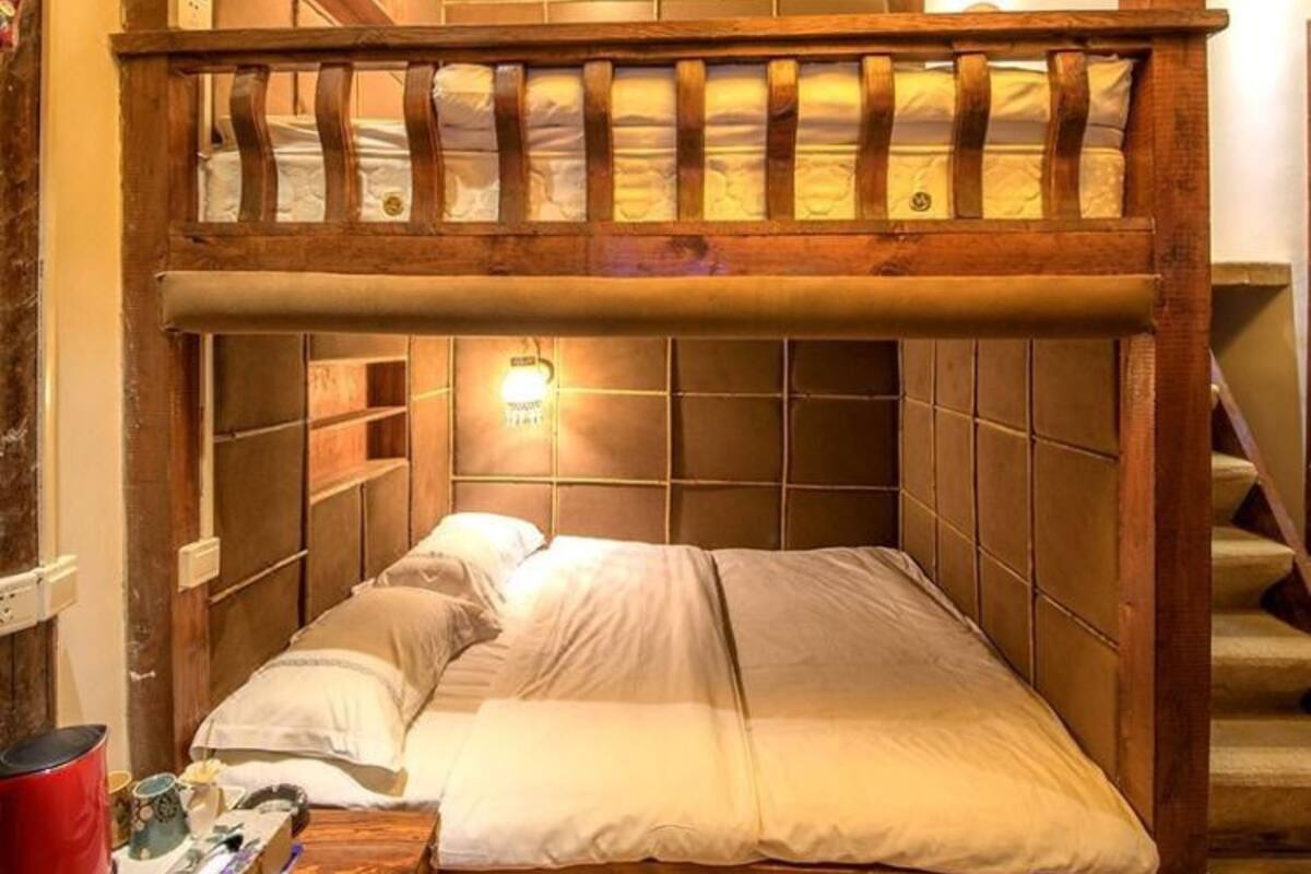 A bunk bed room with a wooden headboard, a bedside table with a red container, and a wall-mounted light fixture.