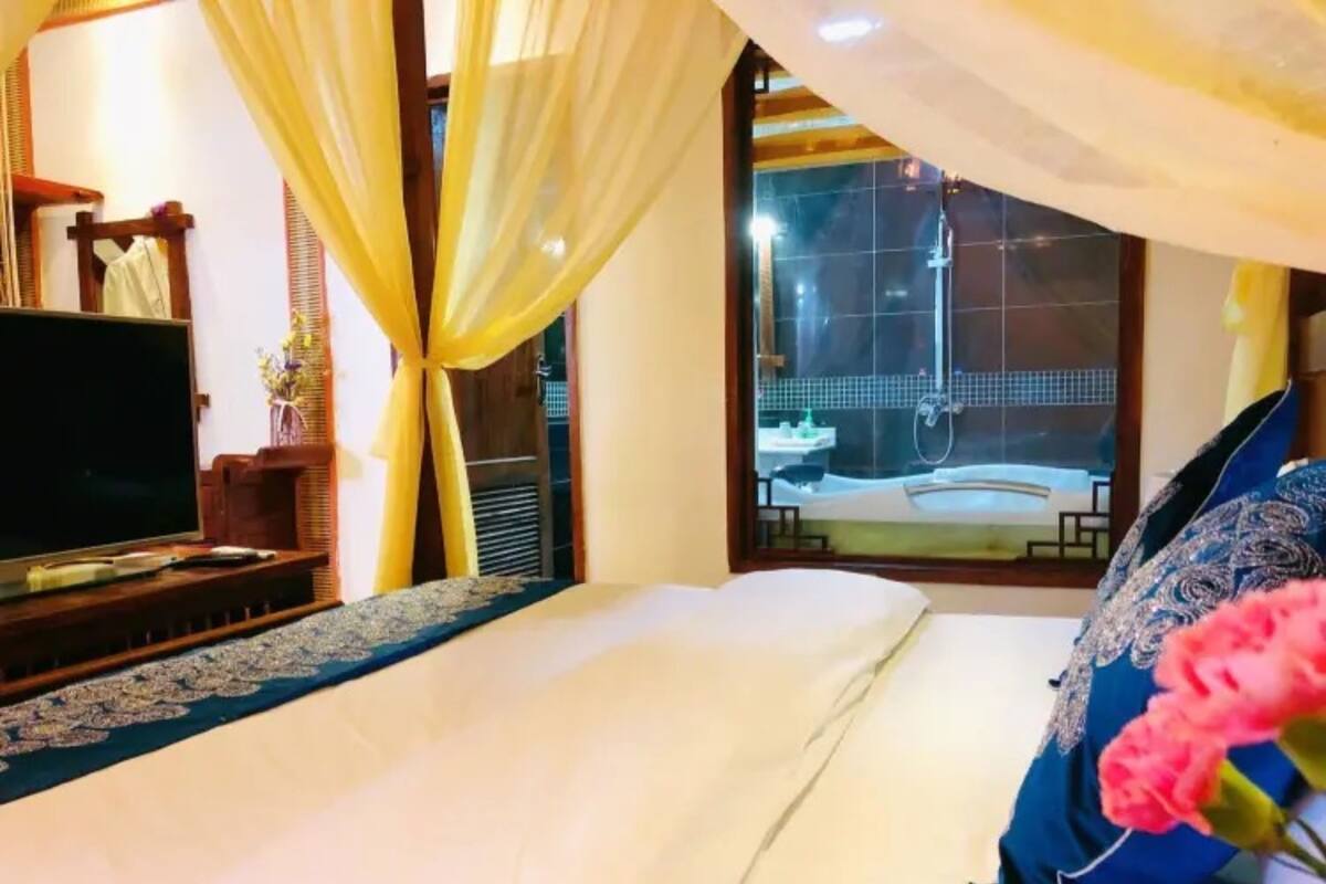 A hotel room with a bed, a TV, a window with curtains, and a view of a spa area.