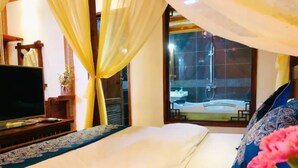 A hotel room with a bed, a TV, a window with curtains, and a view of a spa area.