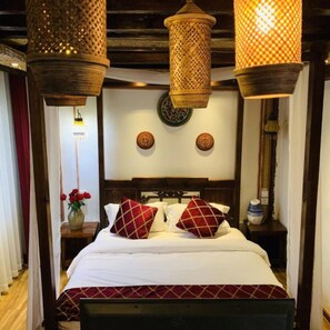 A hotel room with a wooden headboard, a bed with white bedding and red patterned pillows, two wall-mounted decorative plates, and two hanging lanterns.