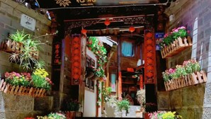 A traditional Chinese gate with a floral hotel sign, potted plants, and red lanterns.