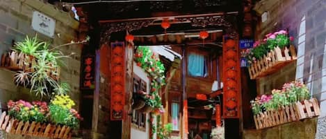 A traditional Chinese gate with a floral hotel sign, potted plants, and red lanterns.