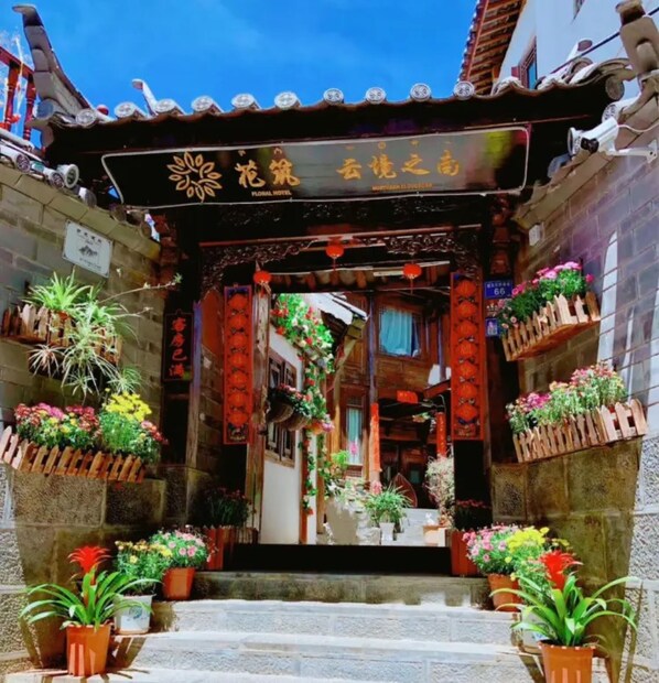 A traditional Chinese gate with a floral hotel sign, potted plants, and red lanterns.