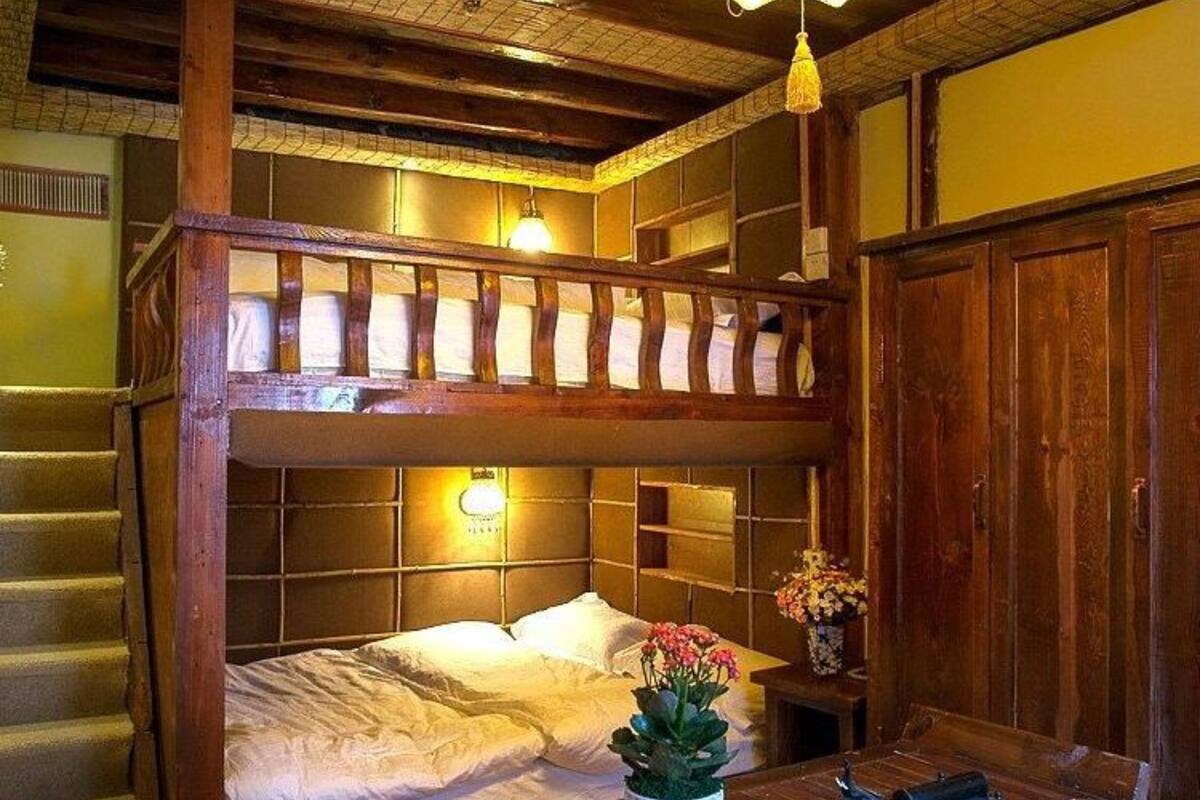 A rustic wooden room with a bunk bed, a small table with a vase of flowers, and a hanging light fixture.