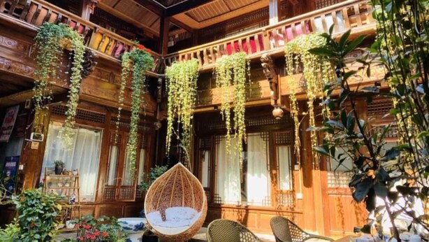 A traditional wooden building with multiple balconies, hanging plants, and a hanging chair.