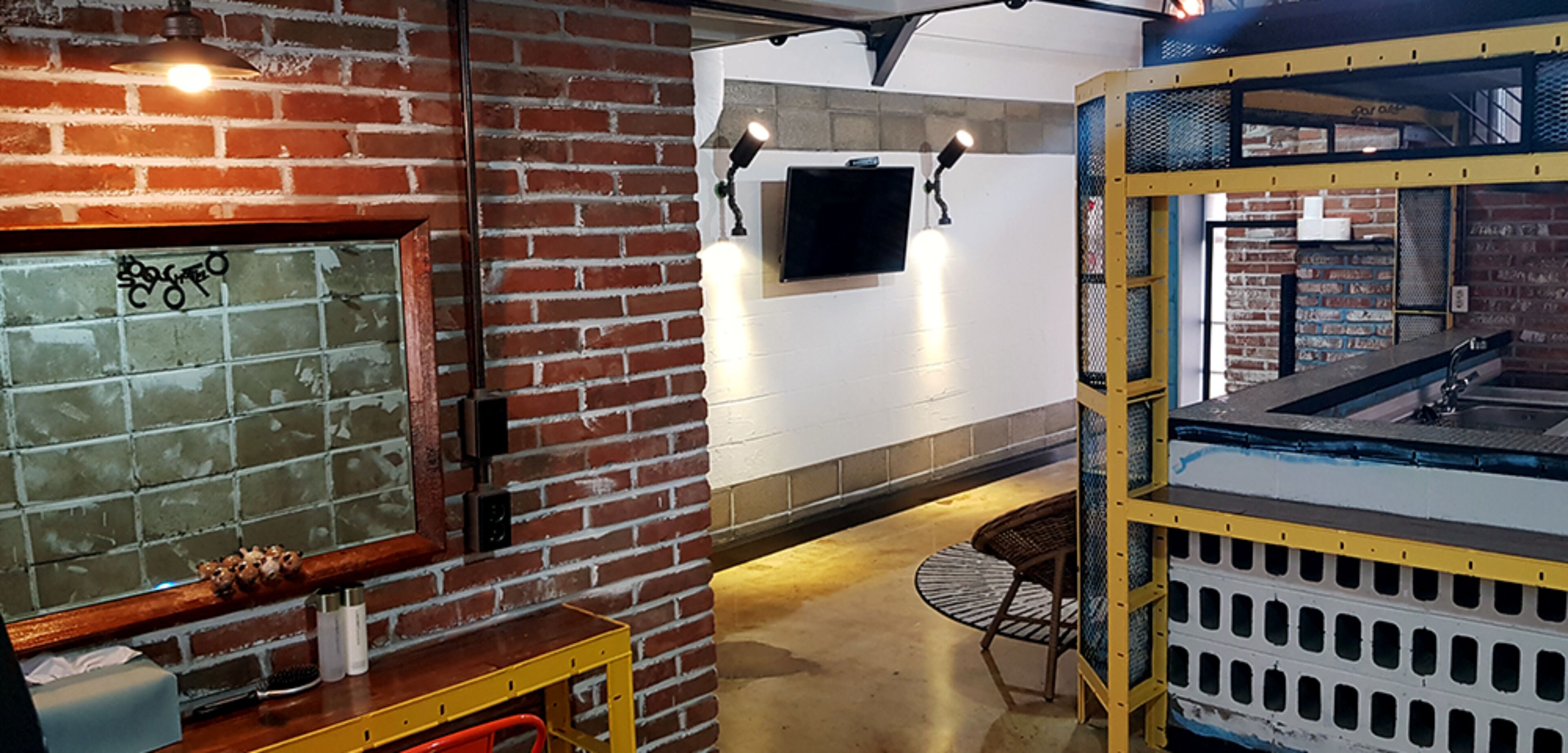 A room with brick walls, a mounted TV, a yellow shelf, and a chair.