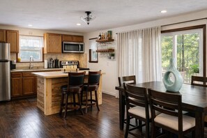A kitchen with wooden cabinets, a microwave, a stove, and a dining area with chairs and a table. - Charming Resort Home. Pet-Friendly! (Tobyhanna)