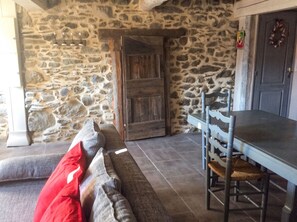 A stone wall interior with a wooden door, a bench with cushions, and a table with chairs.