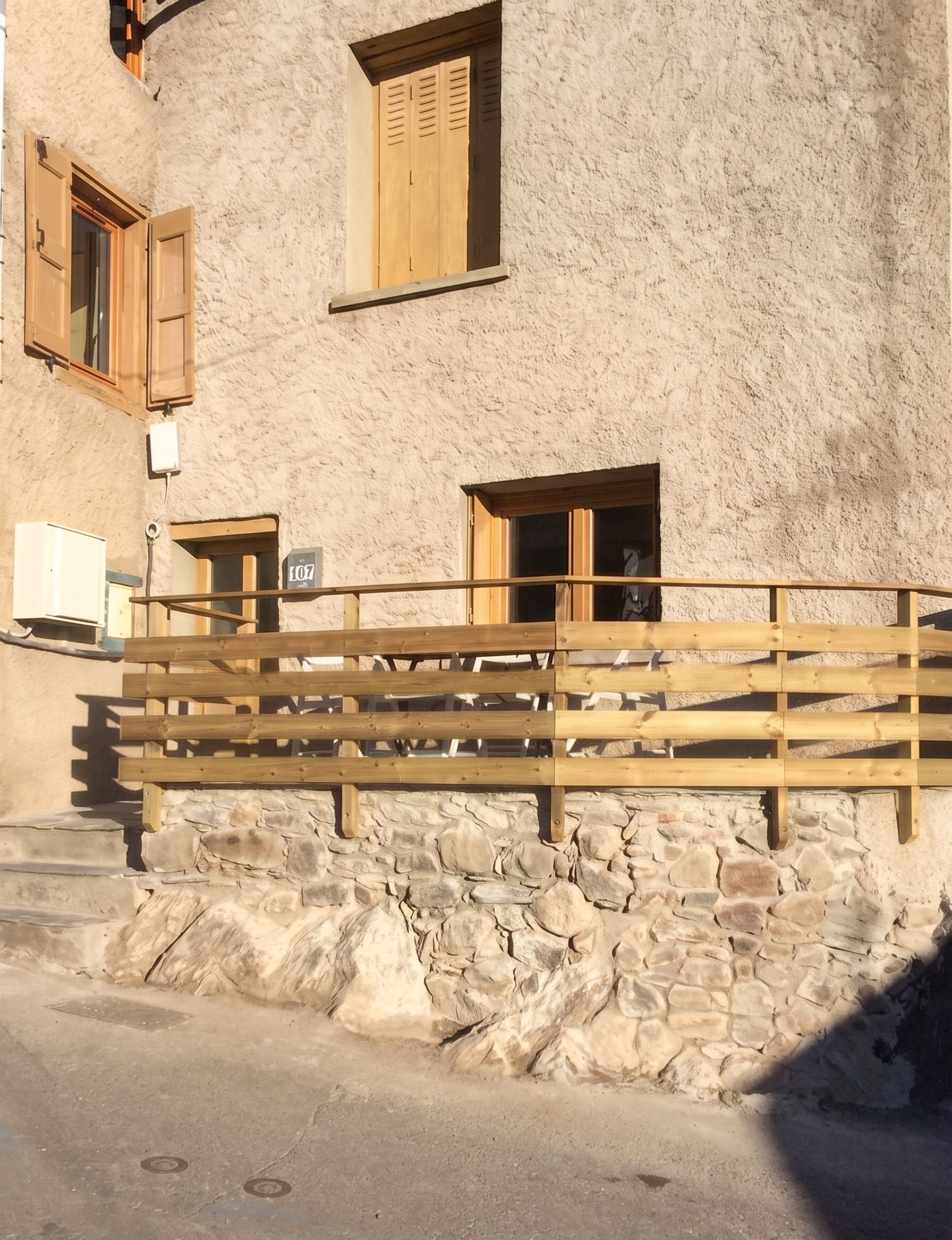 A building with a stone facade, wooden shutters, and a metal railing.