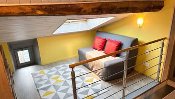 Un dormitorio con techo inclinado, un tragaluz, una cama con almohadas rojas, un tapiz con estampado geométrico y una barandilla de metal.