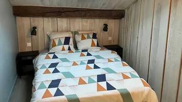 Une petite chambre mansardée, chaleureuse et accueillante, avec un plafond en pente, une lucarne et un lit recouvert d’une courtepointe à motifs géométriques.