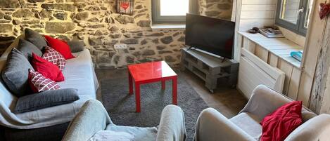 A cozy living room with a stone wall, a sofa, a red table, and a television.