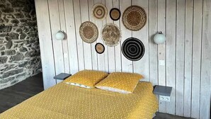 Ein Bett mit gelbem Muster, ein Holzkopfende mit Wandleuchten und eine Steinwand zur Linken.