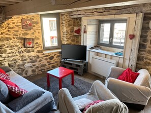 A cozy living room with stone walls, a flat-screen TV, and a small table.