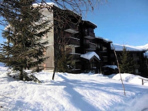 A multi-story lodge with a snow-covered roof and a wooden facade. - Homerez - Apartment in La Plagne (La plagne)