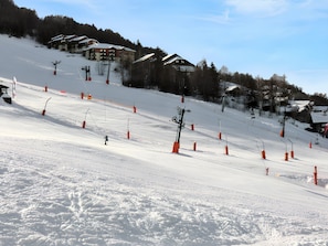 A ski slope with orange safety cones, a ski lift, and buildings in the background. - Homerez - Apartment in La Plagne (La plagne)