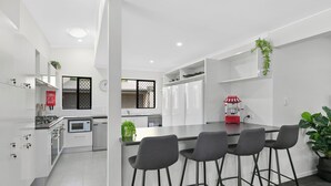 Una cocina moderna con armarios blancos, una isla central con taburetes altos y una máquina de palomitas rojas.