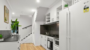 Una cocina moderna con armarios blancos, piso de madera, horno empotrado y refrigerador.