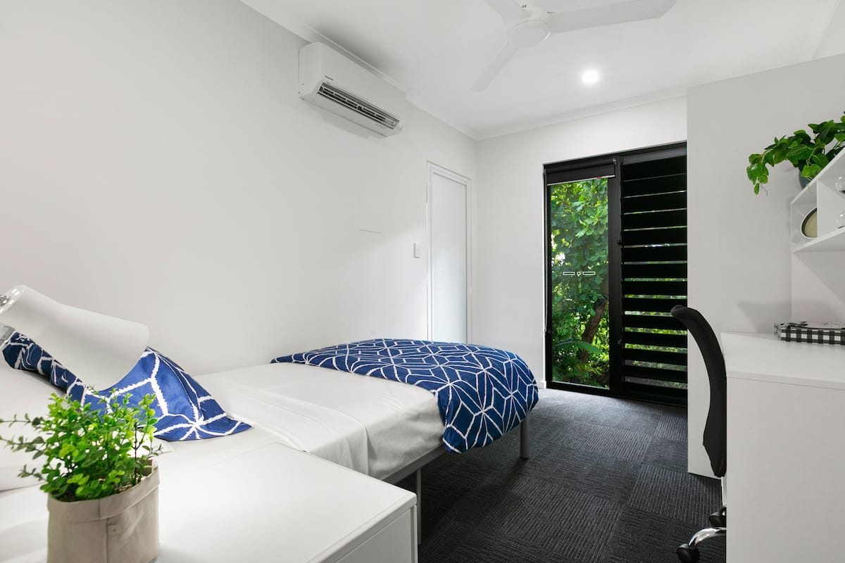 Een moderne hotelkamer met twee bedden, een bureau, een stoel en een potplant.