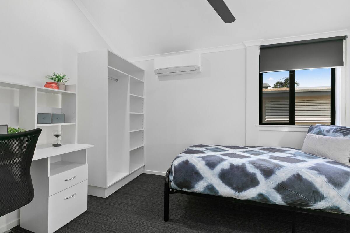 Een slaapkamer met een bed, een bureau, een stoel, een kledingkast en een raam met uitzicht.