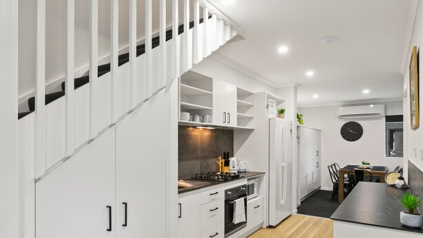 Una cocina moderna con armarios blancos, horno empotrado y comedor con mesa y sillas.
