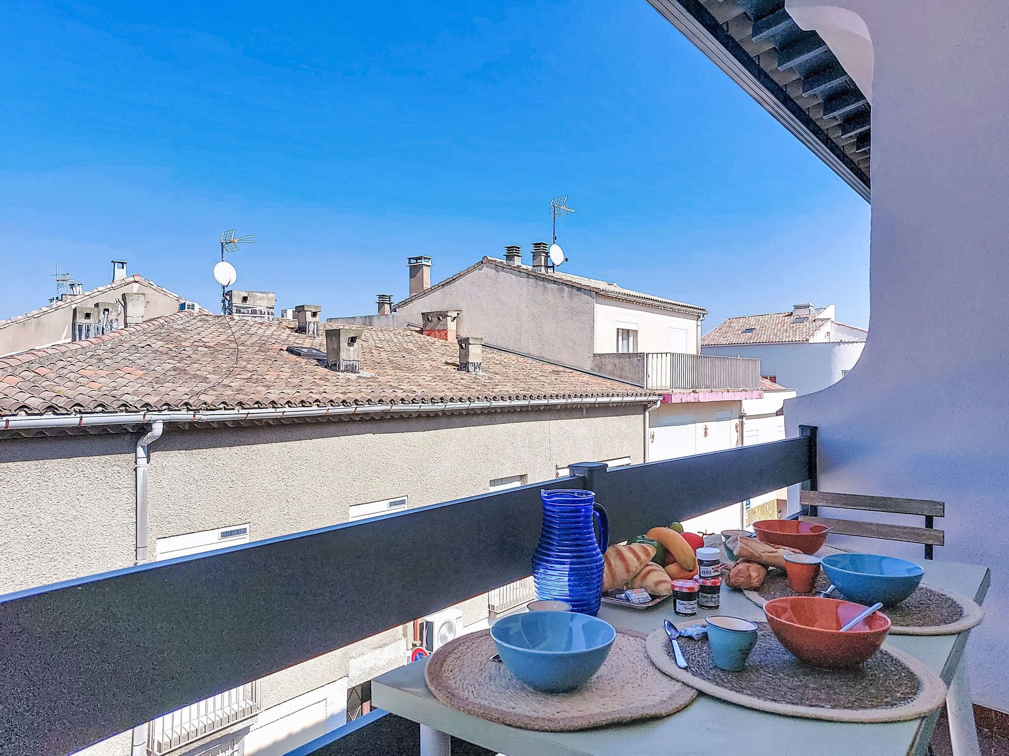 Ein Balkon mit Frühstückstisch, mit Blick auf eine Stadtlandschaft mit Terrakotta-Dächern und Gebäuden.