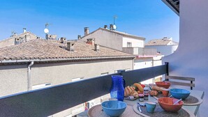 A balcony with a table set for breakfast, overlooking a cityscape with terracotta rooftops and buildings. - Hippocampe by Interhome (Le Grau du Roi)