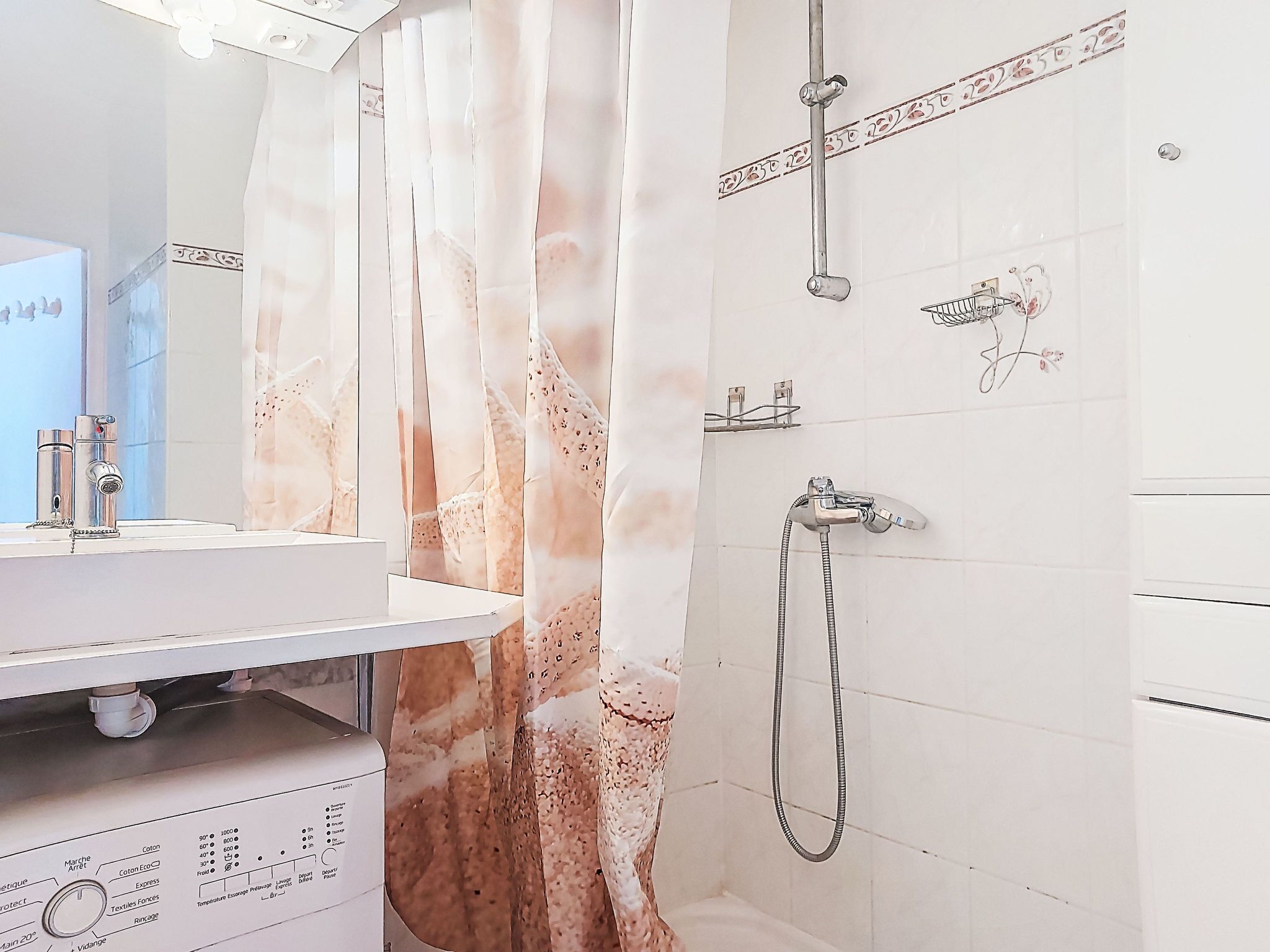 Un baño con lavamanos blanco, ducha con cabezal de ducha de mano y un perchero para toallas.
