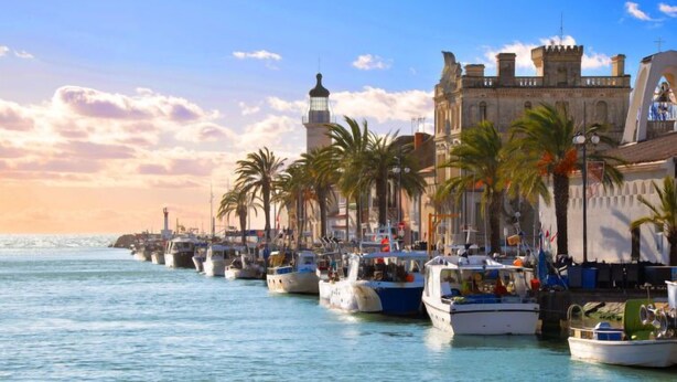 A marina with boats docked, a lighthouse, and a historic building with a castle-like structure. - Hippocampe by Interhome (Le Grau du Roi)