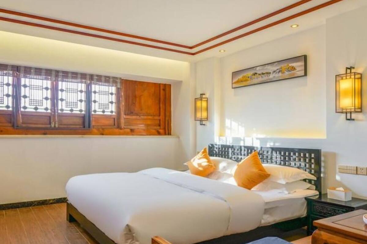 Habitación de hotel con una cama grande, una cama más pequeña, un escritorio con una silla, una ventana con persianas y luces fijadas a la pared.