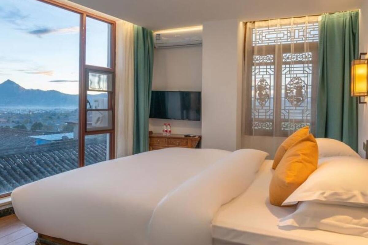 Habitación de hotel con cama, televisor, ventana con cortinas y vistas a la ciudad.