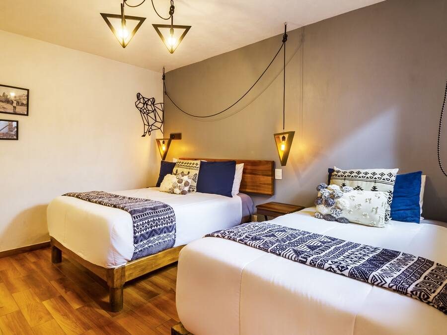 Quarto de hotel com duas camas, soalho de madeira e iluminação na parede.