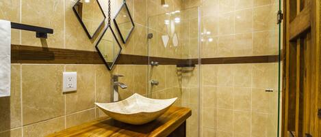A bathroom with a wooden vanity, a beige sink, and a glass shower enclosure.