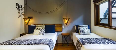 Habitación de hotel con dos camas, suelo de madera y ventana con vistas.