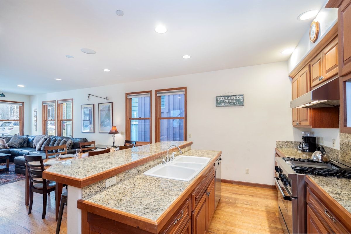 A kitchen with a granite countertop, double sink, wooden cabinets, and a built-in stove.
