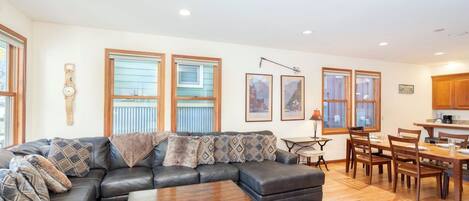 A living room with a sectional sofa, a coffee table, and a dining area with wooden chairs and a table.