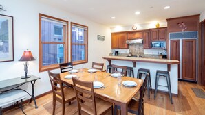 A modern kitchen with wooden cabinets, a central island, and a dining area with a table set for four. - Downtown Telluride Townhome | Walk to Gondola | 3BR, Steam Shower, Parking (Telluride)