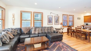A modern living room with a sectional sofa, a wooden coffee table, and a dining area with wooden chairs and a table. - Downtown Telluride Townhome | Walk to Gondola | 3BR, Steam Shower, Parking (Telluride)