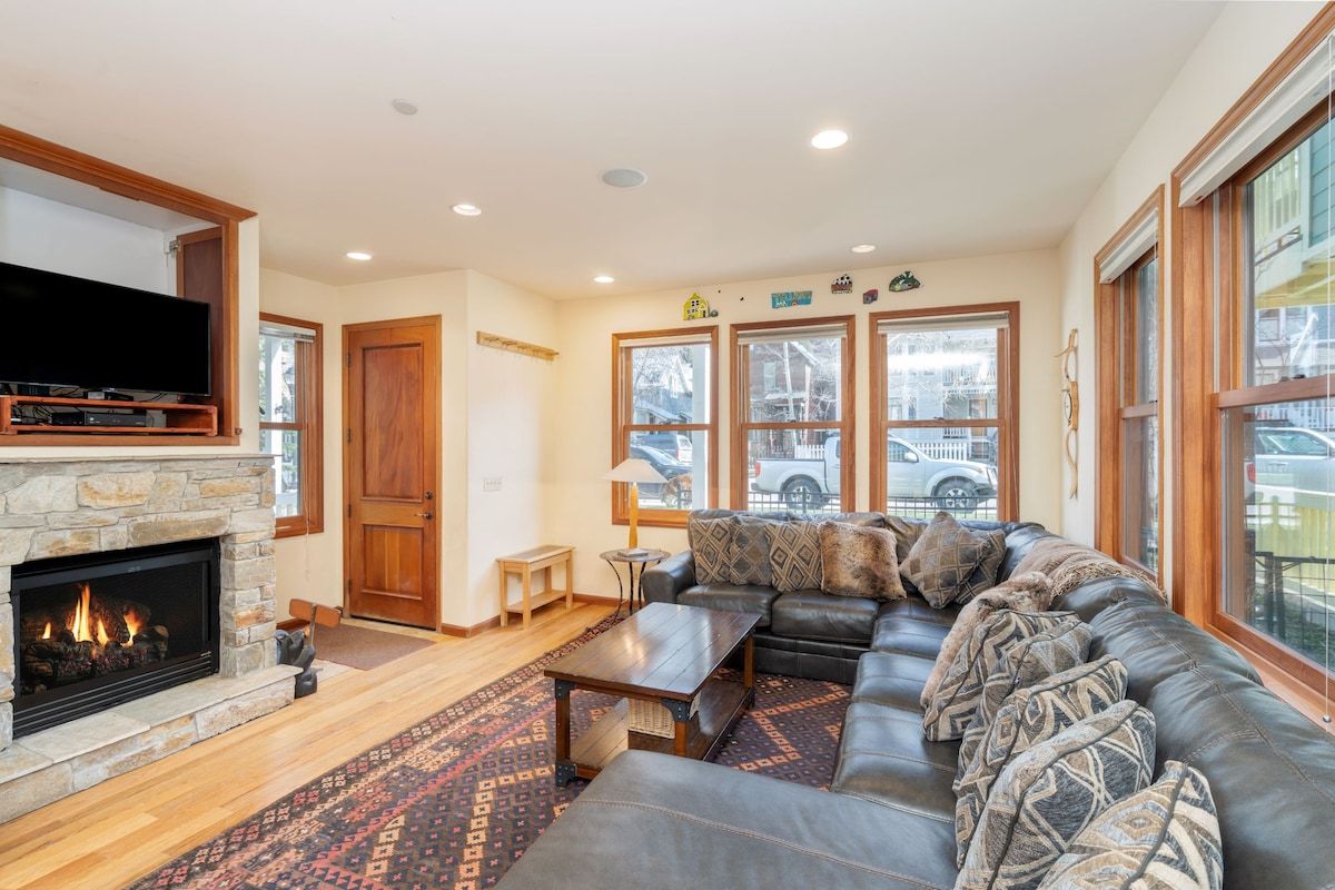 A living room with a stone fireplace, a leather sofa, and a large window with a view of the street.
