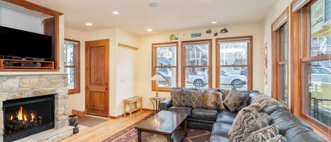 A living room with a stone fireplace, a leather sofa, and a large window with a view of the street.