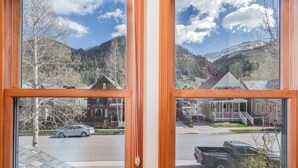 A view through a window with a wooden frame, displaying a street with parked cars, houses, and a mountainous landscape in the background. - Downtown Telluride Townhome | Walk to Gondola | 3BR, Steam Shower, Parking (Telluride)