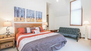 Ein Schlafzimmer mit einem großen Bett, zwei Nachttischen, einem Sessel und einem Kunstwerk an der Wand.